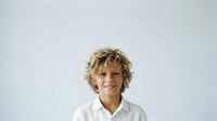 Young boy with curly blonde hair wearing white shirt, smiling at camera against neutral background. Suitable for educational, family, and lifestyle marketing materials.