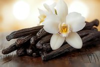 Vanilla pods and orchid flowers on wooden surface with warm golden background for culinary and aromatherapy concepts.
