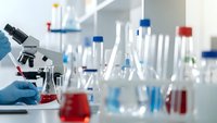 Laboratory scientist in blue gloves conducting research with microscope and colorful chemical solutions in test tubes and beakers for scientific analysis.