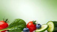 Fresh organic vegetables and fruits arranged on green gradient background with copy space for healthy eating and nutrition concepts.