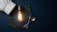 Culinary flat lay with vintage Edison bulb, chef hat, silverware and fresh herbs on dark background for restaurant branding and food service marketing.