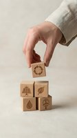 Hand placing wooden cube with recycling symbol on stack of eco-friendly blocks featuring renewable energy icons for sustainable business concepts.