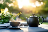 Black teapot and cup set on outdoor table with fresh herbs and blurred garden background, perfect for tea time, wellness, and lifestyle designs.