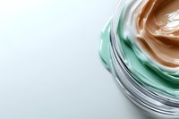 Luxurious skincare cream with swirled green and beige textures in glass jar on white background for beauty and cosmetic product marketing.