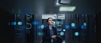Professional Asian woman IT specialist working in modern data center server room with glowing blue network lights and technology equipment.