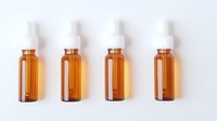 Four amber glass dropper bottles arranged in row on white background, pharmaceutical or cosmetic containers for essential oils, medicine or serum packaging.