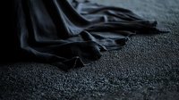 Dark fabric with elegant folds and creases lying on textured carpet surface creates dramatic shadows and contrast in moody atmospheric lighting.