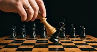 Hand moving wooden chess king piece on checkered board during strategic game play against dark background for business concepts.