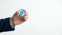 Male hand in business suit holding blue certification badge with checkmark symbol for quality assurance and approval concepts.