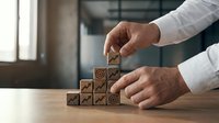 Businessman hands arranging wooden blocks with growth icons in modern office environment representing business development and strategic planning concepts.