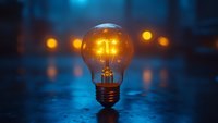 Glowing incandescent bulb with warm filament on blue surface surrounded by blurred lights, representing innovation, creativity, and bright ideas for business and technology concepts.