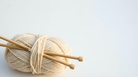 Natural cream wool yarn ball with wooden knitting needles on white background, crafting supplies for handmade projects and textile arts.