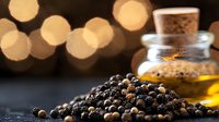 Black peppercorns scattered on dark surface with glass bottle of olive oil and golden bokeh lights in background, macro food photography.