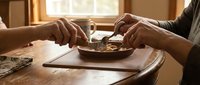 Two people sharing homemade cookies from wooden bowl on rustic table in warm sunlit kitchen creating cozy domestic moment for food photography.