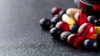 Colorful medical pills and supplements scattered on dark stone background with copy space. Red, yellow and black capsules for healthcare concept.