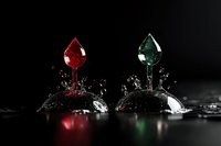 Red and green liquid drops colliding with water surface creating crown splash effect against dark background, dramatic high-speed photography with color contrast.