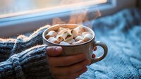 Cozy winter morning with hands holding warm hot chocolate topped with marshmallows by frosted window, perfect for seasonal comfort and hygiene concepts.