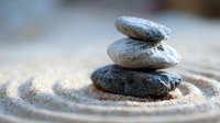 Balanced zen stones pyramid on sand with circular pattern, creating peaceful meditation atmosphere. Wellness and spa concept for mindfulness practice.