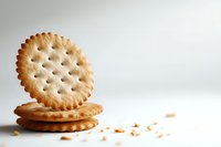Round crispy crackers stacked with holes and crumbs scattered on white surface, minimalist food photography for packaging design and advertising.