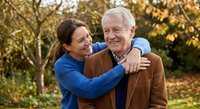 Happy mature Caucasian couple embracing outdoors in autumn park with golden foliage. Senior man and woman sharing affectionate moment during fall season walk.