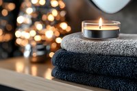 Burning aromatic candle on folded soft towels with blurred golden bokeh lights creating cozy spa atmosphere for relaxation and wellness treatments.