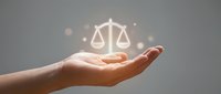 Hand holding glowing scales of justice symbol with light effects on neutral background representing legal services and law concept.