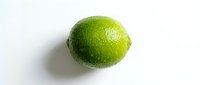 Fresh green lime with textured skin and water droplets on white background, suitable for food, beverage, and culinary design projects.