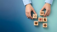 Hands arranging wooden blocks with healthcare, medical, and financial symbols on blue and turquoise background. Concept for insurance, wellness planning, and health coverage.
