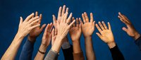 Diverse group of hands raised up together against blue background showing unity, teamwork and collaboration in business or community setting.