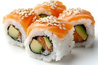 Fresh salmon and avocado sushi rolls topped with raw fish and sesame seeds on white background, traditional Japanese cuisine preparation.