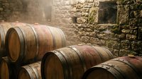 Wooden wine barrels stacked in a stone cellar with aged walls, suitable for winery, vineyard, wine production, and beverage industry marketing materials.