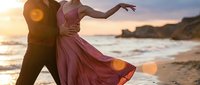 Romantic couple dancing on beach at sunset with flowing dress and golden hour lighting creating dreamy atmosphere for wedding or engagement concepts.