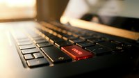 Close-up of laptop keyboard with glowing red enter key, shallow depth of field, warm lighting creating professional workspace atmosphere for business concepts.