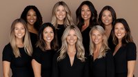Diverse group of women wearing black tops smiling at camera against neutral background, professional headshots style portrait for business or beauty industry.