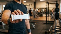 Caucasian male athlete in black t-shirt wrapping wrist with white athletic tape in gym setting. Fitness preparation and injury prevention concept for sports training and workout routines.