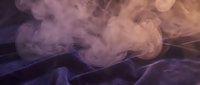 Soft pink and purple smoke swirling above dark blue velvet fabric, creating a moody, atmospheric scene with elegant texture contrast.