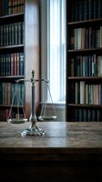 Brass scales of justice on wooden desk in law library with books and window light for legal education and attorney office concepts.
