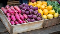 Fresh organic produce in rustic wooden crate featuring vibrant pink radishes, purple beets, and yellow lemons with green herbs, showcasing farmers market fresh vegetables.