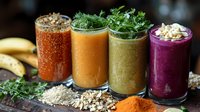 Four colorful healthy smoothies in glasses with fresh herbs, seeds and nuts toppings. Nutritious breakfast drinks with natural ingredients for wellness lifestyle.