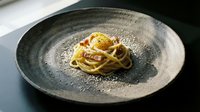 Spaghetti carbonara with egg yolk, crispy bacon, and parmesan on a rustic dark ceramic plate, elegant restaurant presentation.