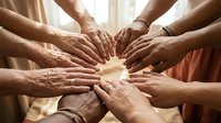Diverse group of people joining hands together in a circle, symbolizing unity, teamwork, and community support in a warm indoor setting.