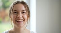Young Caucasian woman laughing joyfully with genuine smile showing teeth in bright natural light indoor setting for lifestyle and wellness content.
