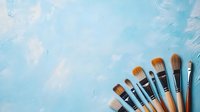 Professional makeup brushes arranged in diagonal line against light blue textured background with copy space for beauty and cosmetic industry content.