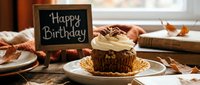 Autumn birthday cupcake with whipped cream topping and pecans on rustic wooden table beside a chalkboard Happy Birthday sign.