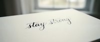 Stay strong written in cursive on white paper with window and blurred background, motivational quote for inspiration and encouragement.