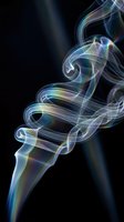 Colorful iridescent smoke swirls elegantly against a dark black background, creating abstract flowing curves with rainbow hues for creative design.