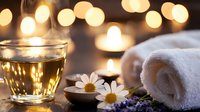 Relaxing spa composition with herbal tea, chamomile flowers, lavender and white towel against warm bokeh lights background, wellness and aromatherapy concept.