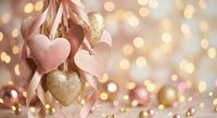 Romantic pink and gold heart decorations hanging with ribbons against warm bokeh lights background for Valentine's Day, wedding or anniversary celebrations.