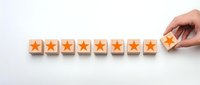 Hand placing wooden cube with orange star completing row of eight rating blocks on white background for customer feedback and quality assessment.