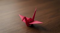 Red origami paper crane folded from traditional Japanese paper art sitting on dark wooden surface for craft and cultural projects.